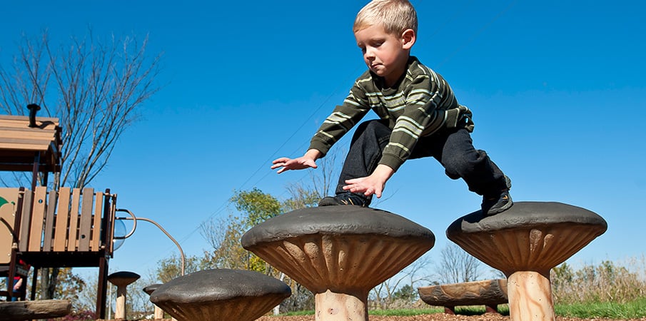 A young boy steps from one mushroom stepper to the next.
