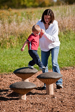 A mother holds her sons hand as she helps him step on the mushroom top steppers.