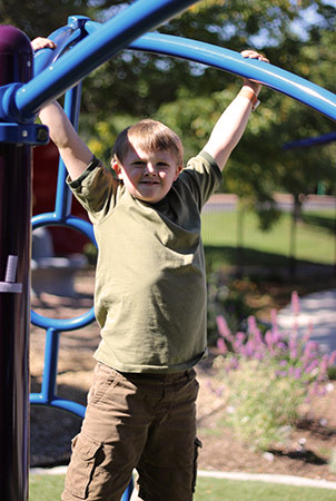 A boy hangs from a blue overhead monkey bar structure. 