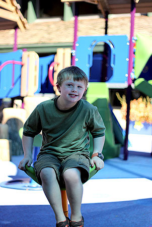 A little boy sits on a chair spinner and smiles. 