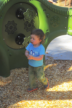 Little boy walks past a green play panel. 