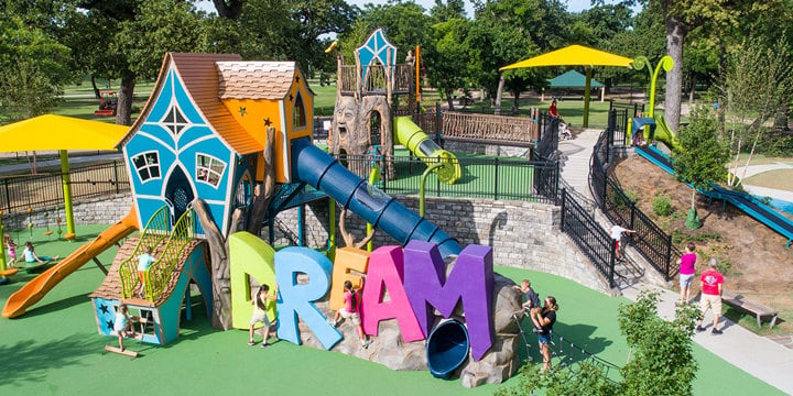 Brightly colored cartoon-like playground with turquoise house-shaped central climbing structure and the word "dream" in bright colors located under the house. 