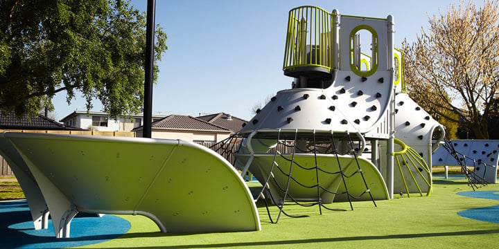 A futuristic-looking playground with a silver mobius climbing wall with a net structure leading up to it and other playground components in bright green and blue. 