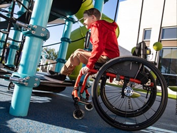 A boy in a wheelchair prepares to transfer to disc net climber, which illustrates inclusive playground design 